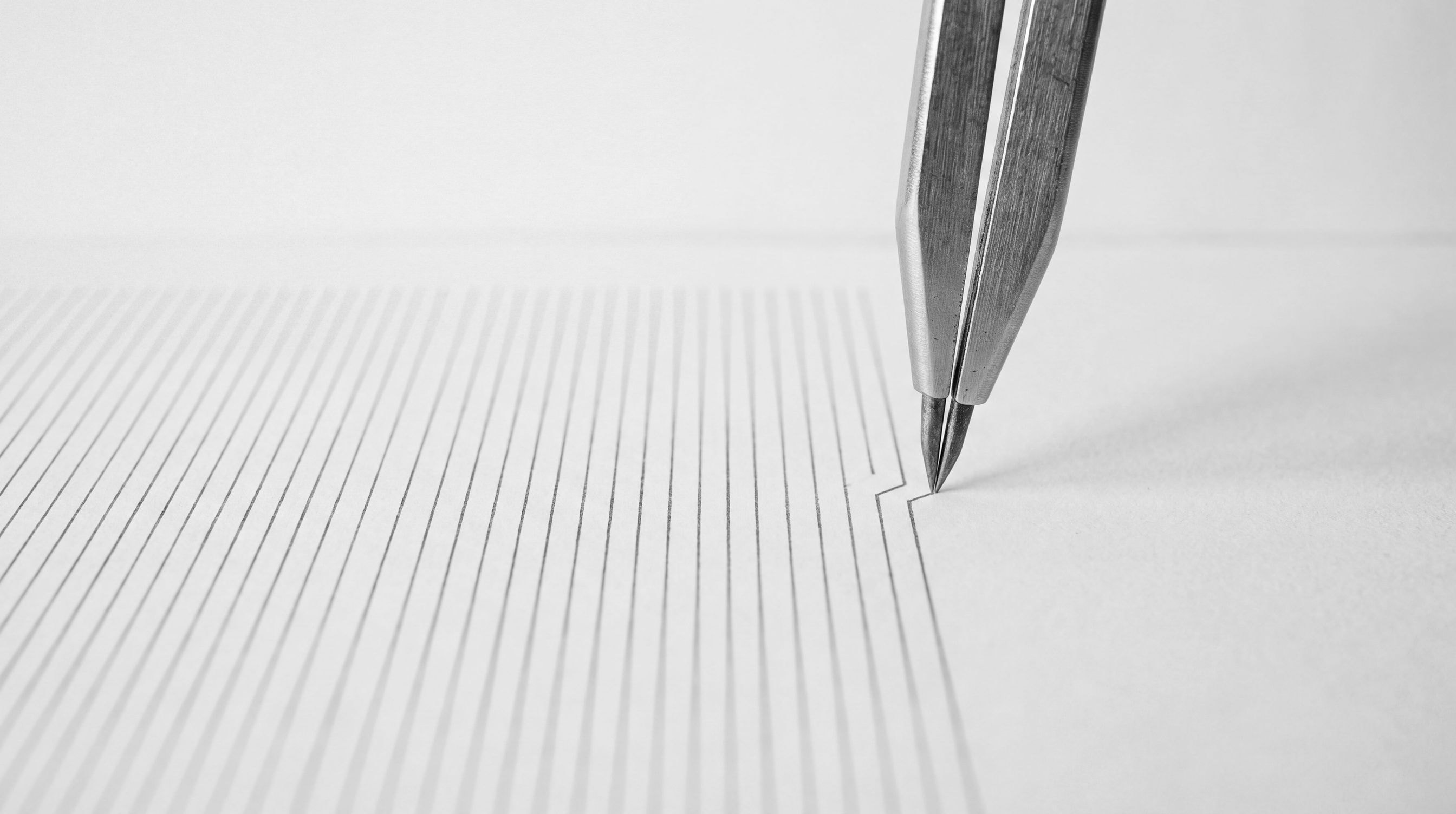A steel drafting divider resting its point on the one place where a ruled line steps out of alignment with its neighbours, on matte paper
